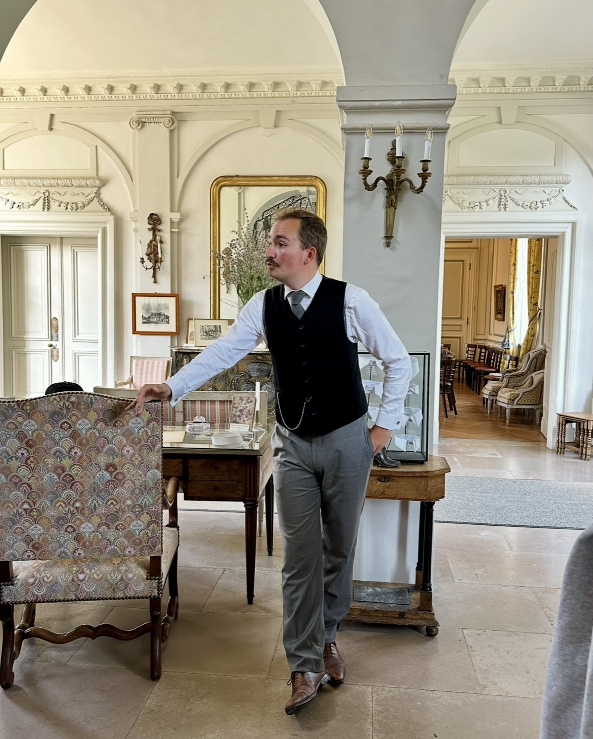 Photo du guide du château de Miromesnil accoudé sur un fauteuil d'époque dans la salle principale