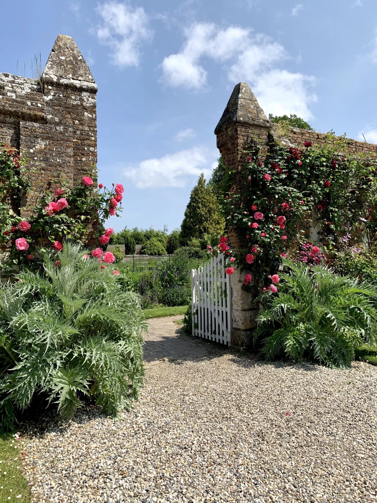 Entrée fleurie du jardin potager du Château de Miromesnil avec murs anciens, roses et portail blanc