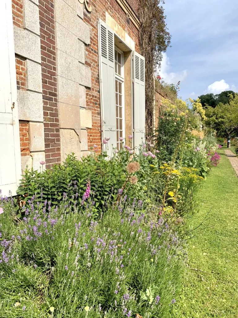 Façade en briques du Château de Miromesnil bordée de massifs fleuris et d’une allée de jardin